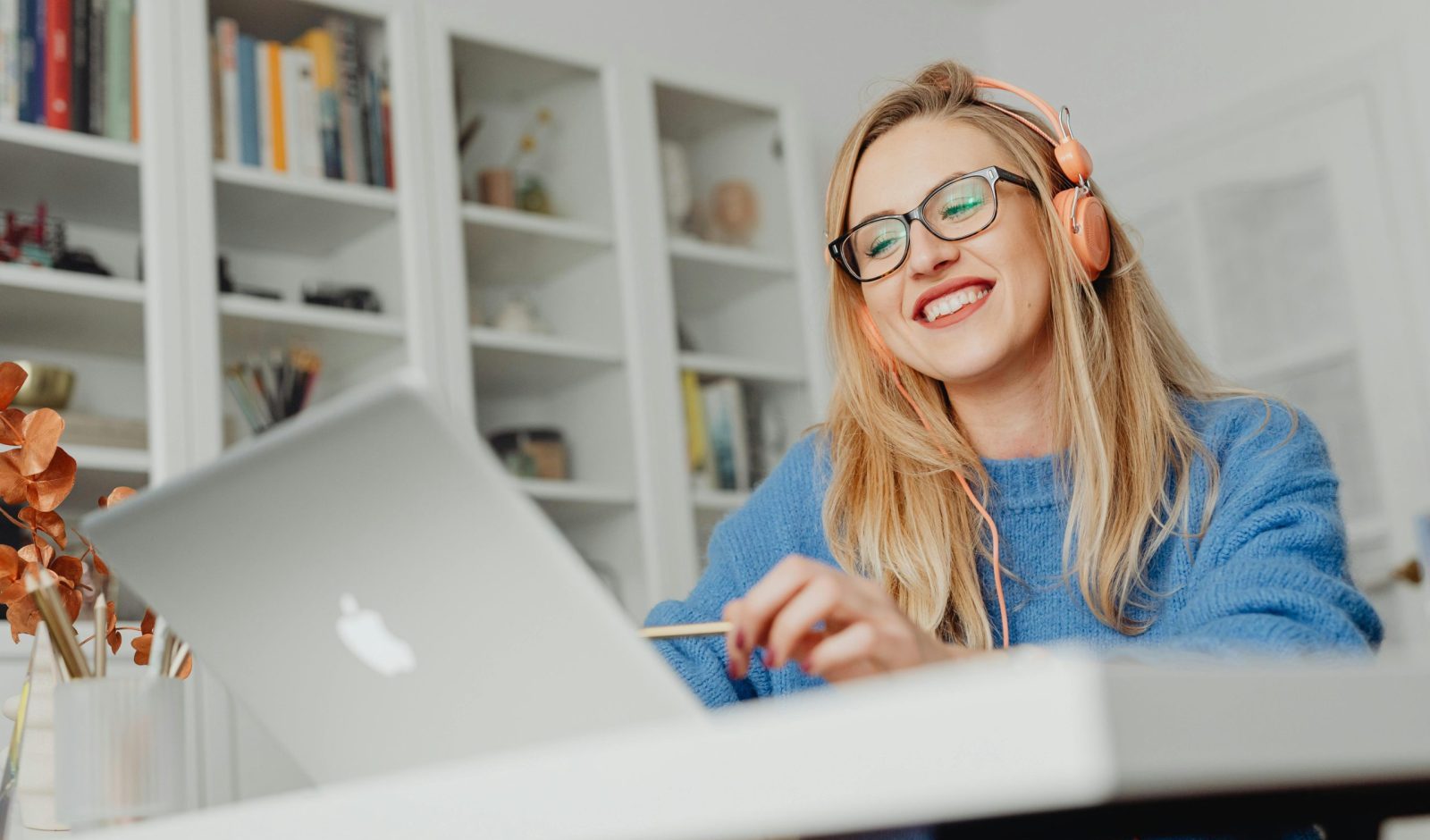 Smiling woman wearing eyeglasses and headphones, working at home on a laptop.