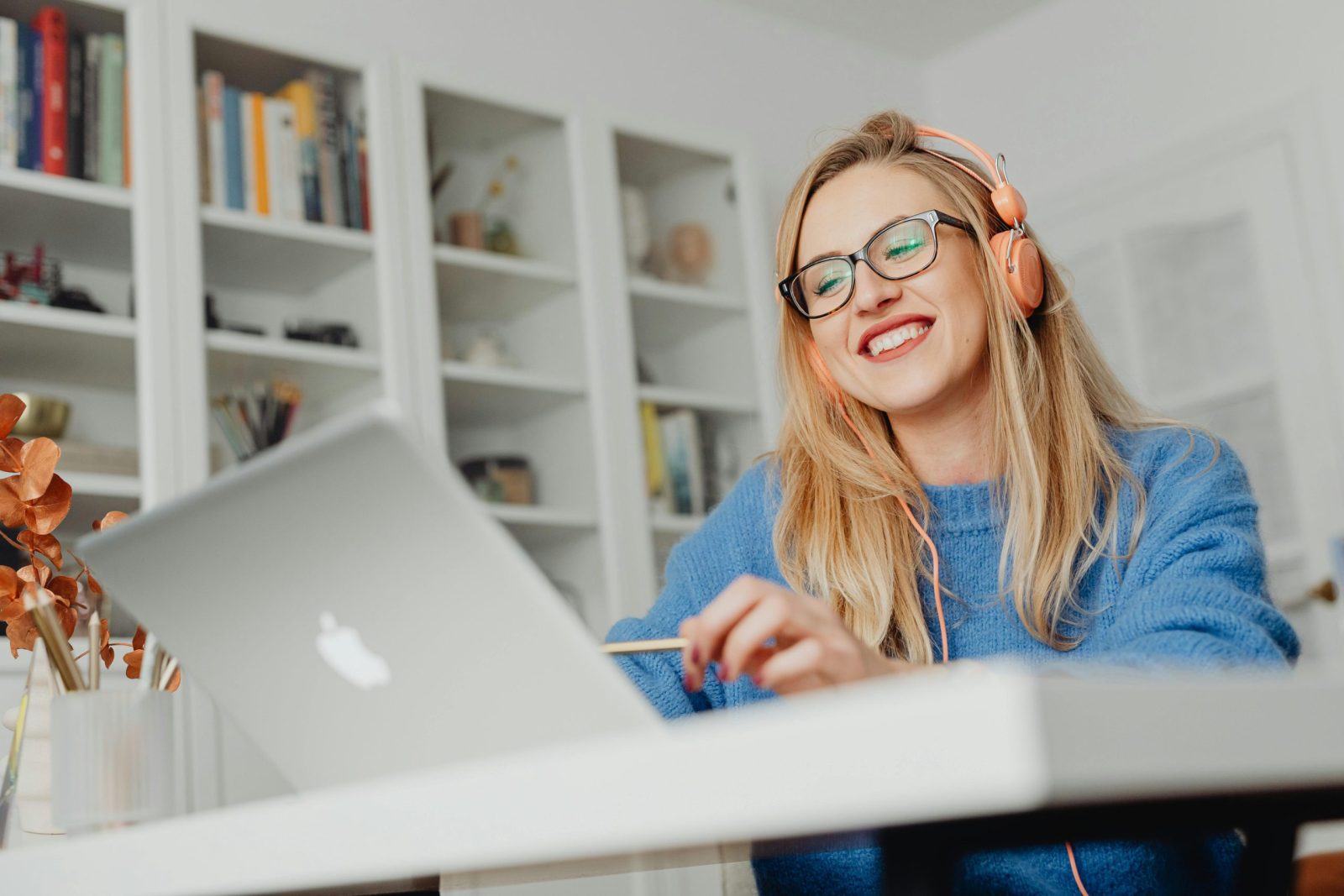 Smiling woman wearing eyeglasses and headphones, working at home on a laptop.